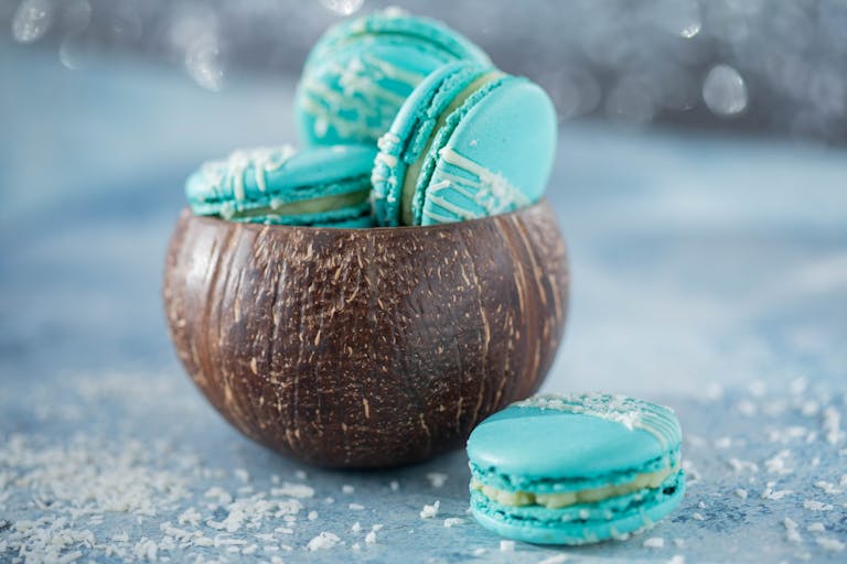Blue macarons in a coconut shell on a blue background. Delectable and colorful dessert presentation.