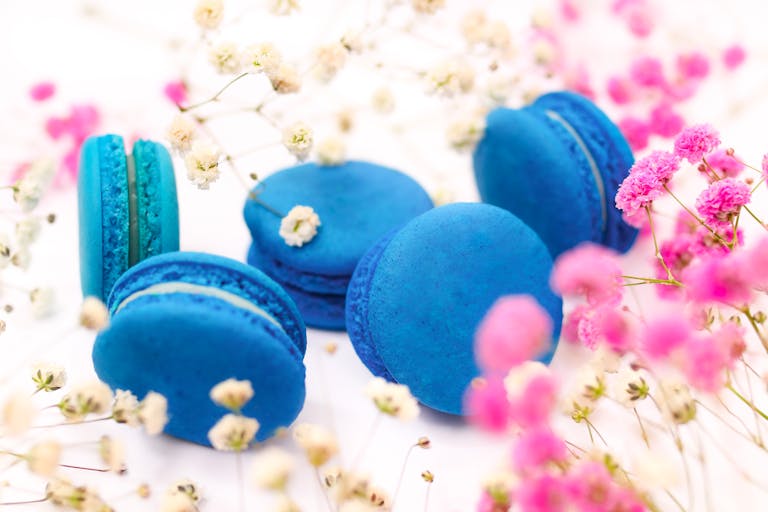 Blue macarons surrounded by pink and white flowers on a bright background.