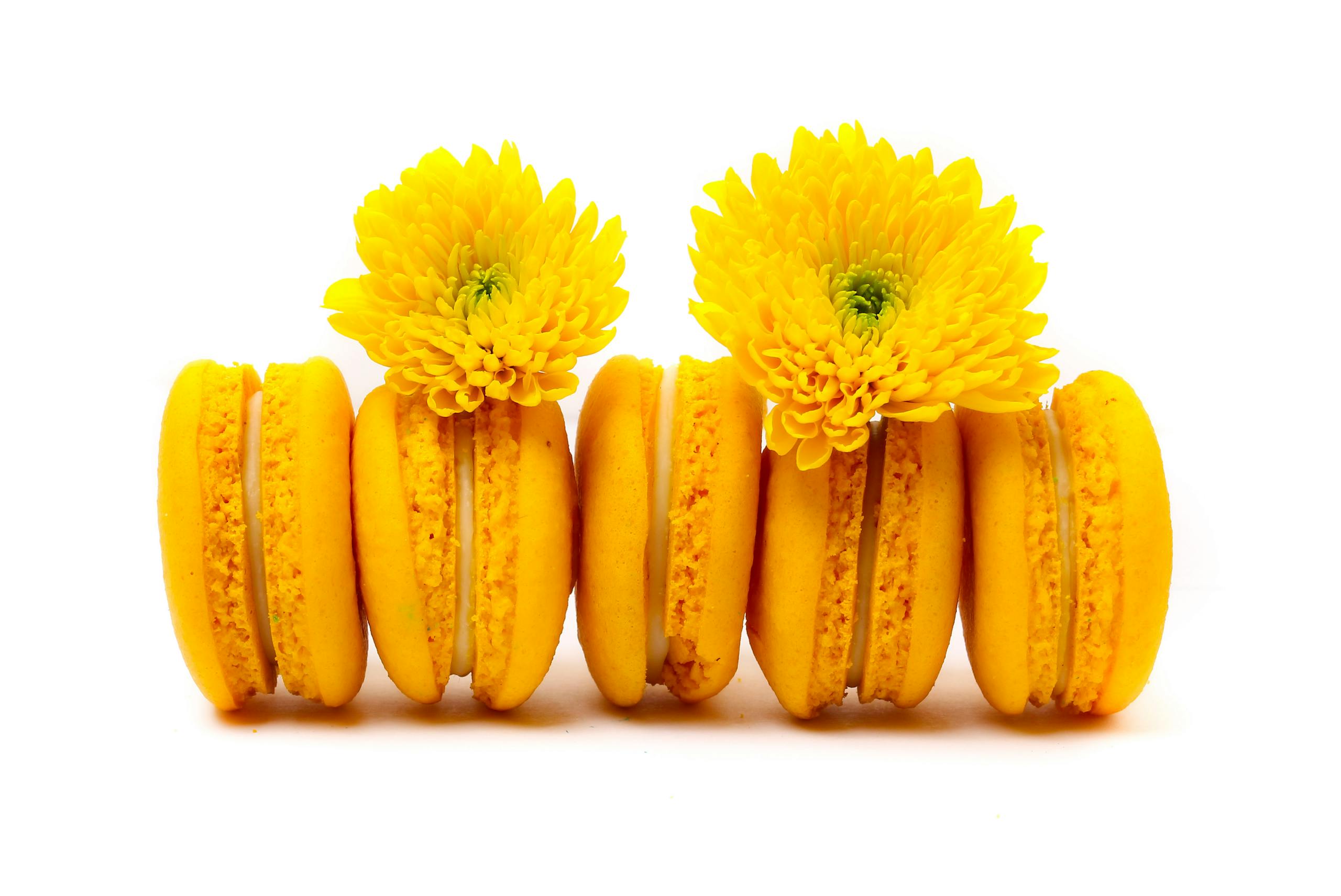 Bright yellow macarons paired with chrysanthemums on a white background.