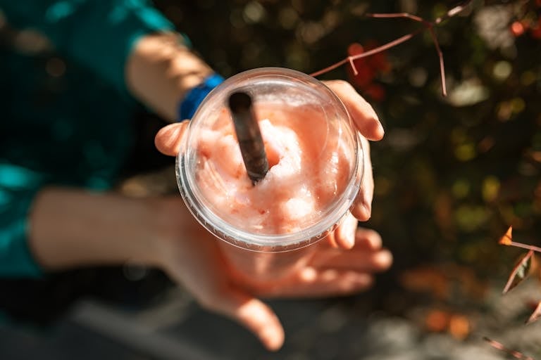 Close-up of a hand holding a refreshing strawberry smoothie in sunlight.