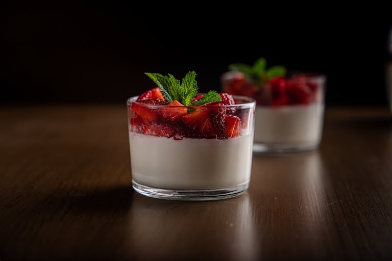 Close-up of creamy panna cotta topped with fresh strawberries and mint, served in a glass.