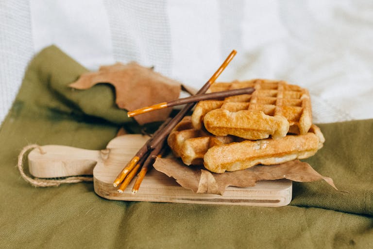 Delicious homemade waffles with chocolate sticks on a rustic wooden board, perfect for a cozy autumn treat.