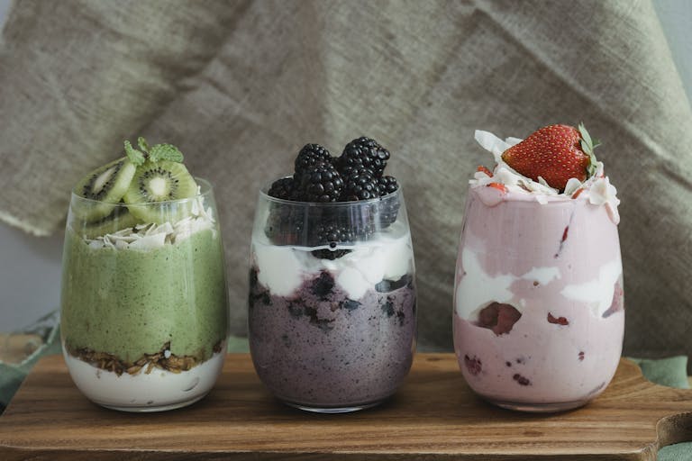 Delicious yogurt parfaits with kiwi, blackberries, and strawberries on a wooden board.